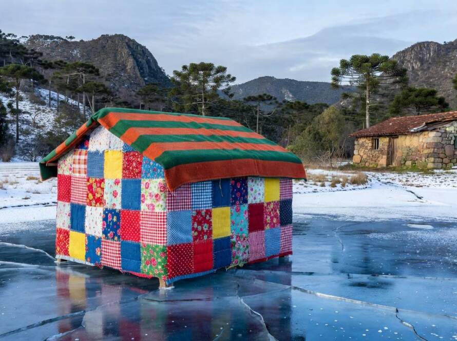Instalação artística de cabana de colchas em lago congelado na região sul do Brasil, com paisagem invernal e araucárias.