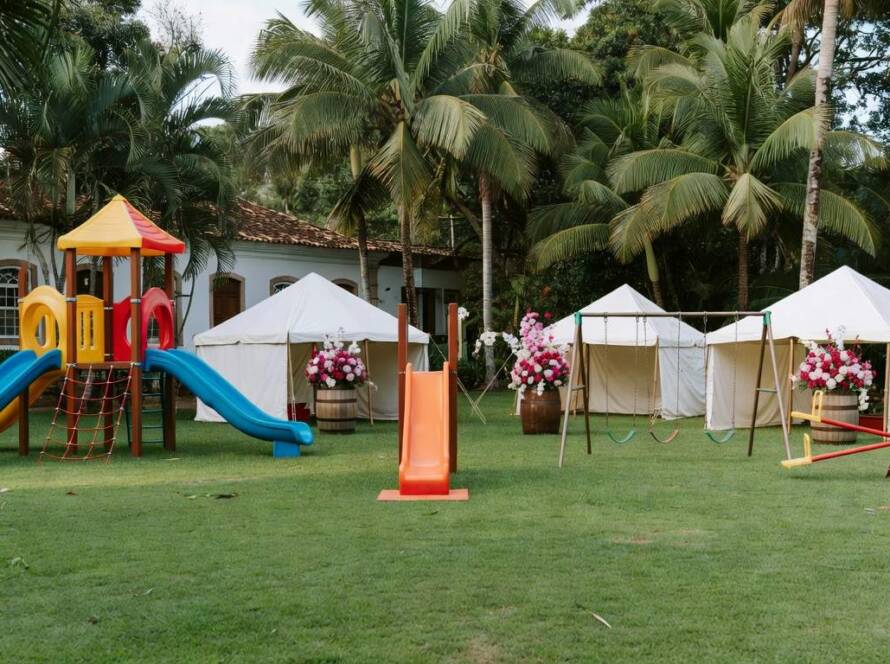Gramado de casamento transformado em playground interativo em jardim tropical brasileiro, com brinquedos e tendas.